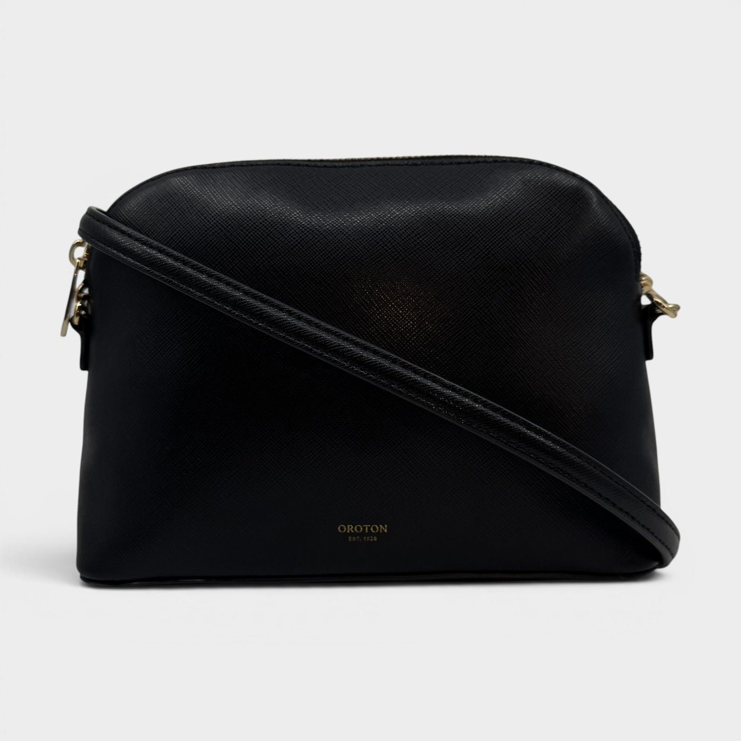 A black textured leather crossbody bag with a gold-tone logo on the front and gold hardware, shown against a light gray background.