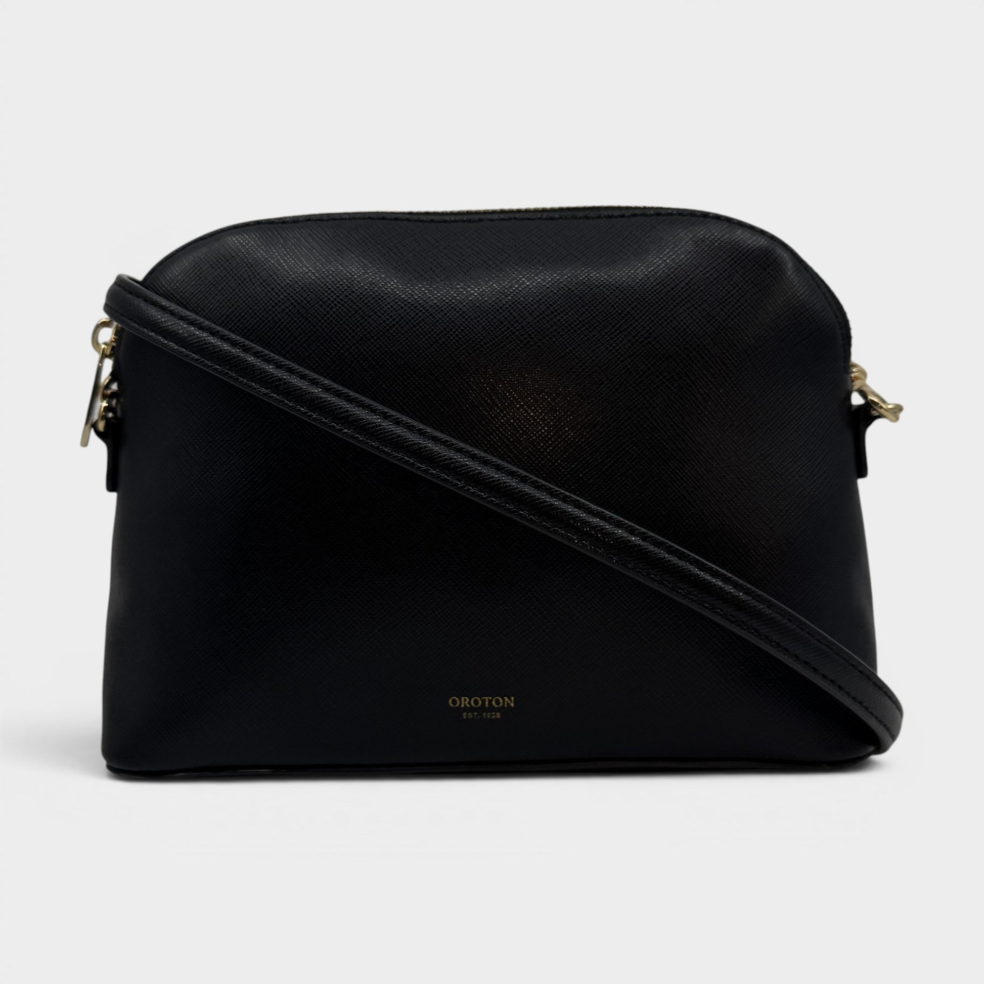 A black textured leather crossbody bag with a gold-tone logo on the front and gold hardware, shown against a light gray background.