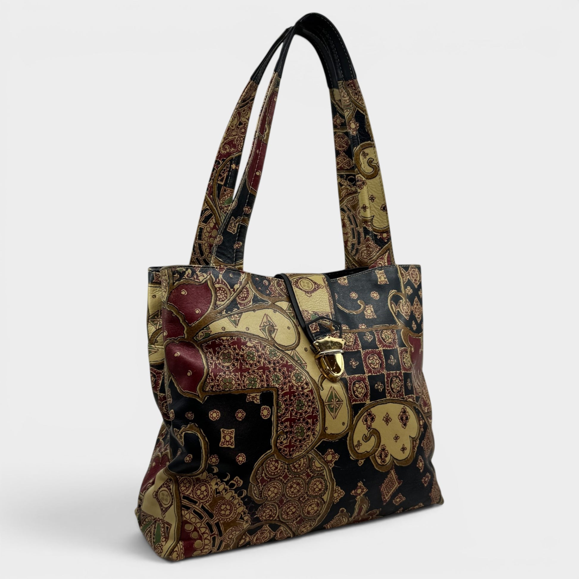 A structured tote bag featuring an intricate vintage-style playing card pattern in black, gold, and deep red, with a gold-tone buckle closure on the front flap.