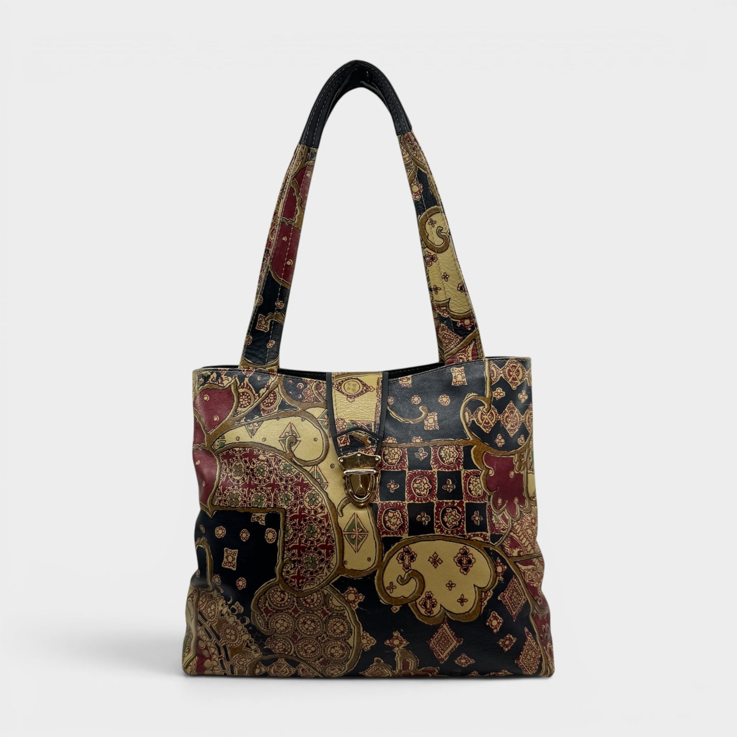 A structured tote bag featuring an intricate patchwork design of traditional Indian motifs, including paisley and floral patterns in gold, red, and navy blue, with dark navy handles.