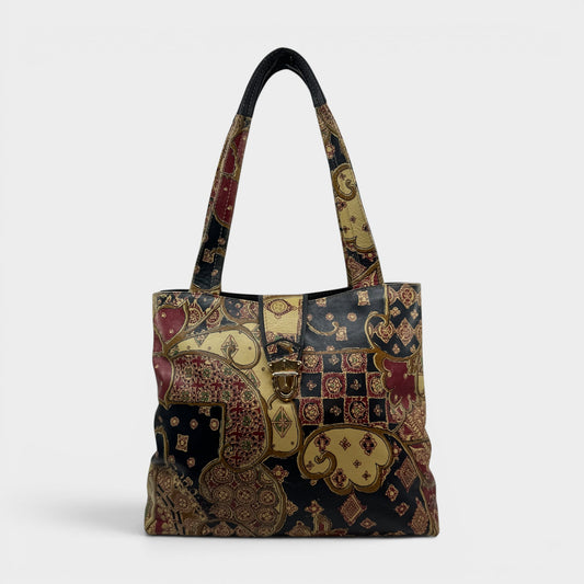 A structured tote bag featuring an intricate patchwork design of traditional Indian motifs, including paisley and floral patterns in gold, red, and navy blue, with dark navy handles.