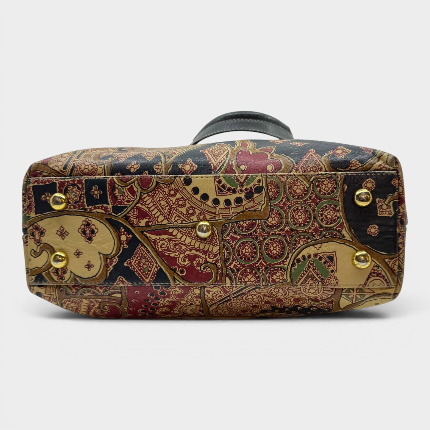 A rectangular handbag with a highly detailed, ornate paisley and floral pattern in gold, red, navy, and beige, featuring gold-tone metal studs and a dark gray handle, shown against a light gray background.